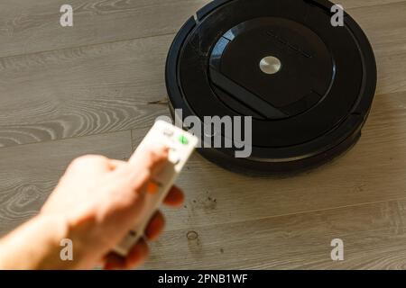 Femme avec téléphone portable et robot-aspirateur moderne à télécommande sur le sol dans la chambre. Banque D'Images