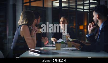 Commençons ce quart de nuit. un groupe diversifié d'hommes d'affaires assis ensemble et ayant une réunion au bureau tard dans la nuit. Banque D'Images