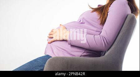 Une fille enceinte s'assoit dans une chaise et se tient à l'estomac. Le concept de fatigue et de malaise pendant la grossesse. Posture assise inconfortable, hormo Banque D'Images