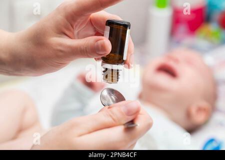 La mère goutte des gouttes de coliques dans l'estomac d'un petit enfant. Banque D'Images