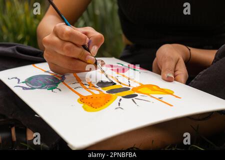 Artiste anonyme de sexe féminin utilisant un pinceau tout en peignant l'abeille sur une feuille de papier blanc avec du liquide noir Banque D'Images