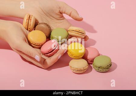 Femme méconnaissable avec manucure prenant pile de délicieux macarons multicolores de surface rose Banque D'Images