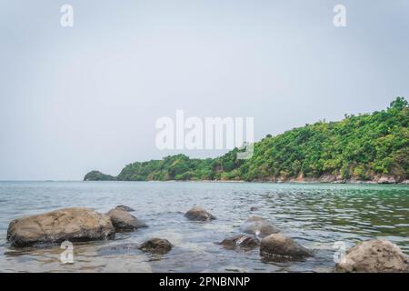 Une vue panoramique sur un plan d'eau, avec des rochers déchiquetés qui jerrent de la surface et des arbres et de l'herbe luxuriants sur le rivage Banque D'Images