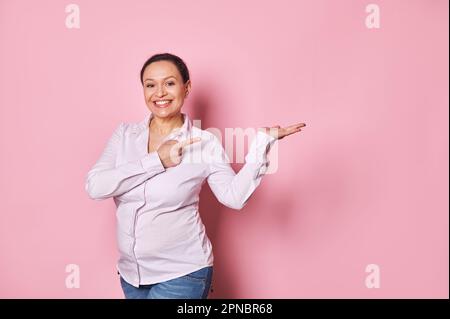 La femme enceinte sourit à la caméra pointe son index vers l'espace de copie de sa main paume vers le haut. Gynécologie maternité Pegnancy Banque D'Images