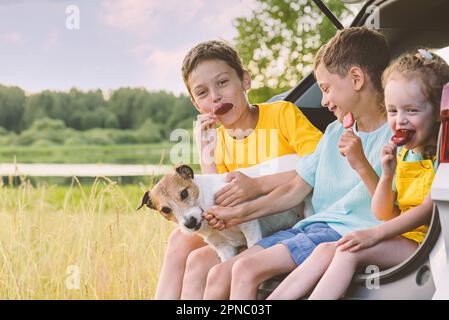 Famille voyageant en voiture ayant pique-nique dans la nature. Enfants souriants mangeant de la popsicle Banque D'Images