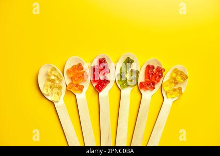 Composition à plat avec de délicieux bonbons d'ours en gelée dans une cuillère en bois, ours en gelée sur fond jaune, vue de dessus, espace de copie. Banque D'Images