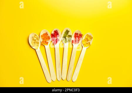 Composition à plat avec de délicieux bonbons d'ours en gelée dans une cuillère en bois, ours en gelée sur fond jaune, vue de dessus, espace de copie. Banque D'Images