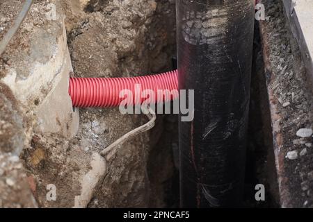 Ondulé pour câble d'isolation de fils souterrains, tubes en plastique, gros tuyau noir avec isolation pour l'eau, tuyau d'ondulation rouge avec espace de copie. Travaux souterrains, fils et communications. Banque D'Images