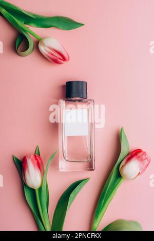 Bouteille de parfum et fleurs de tulipe sur fond rose. Vue de dessus, plan d'agencement, maquette. Banque D'Images