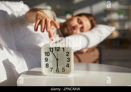 L'homme endormi atteint sa main pour éteindre le réveil qui sonne le matin Banque D'Images