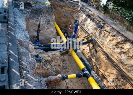 Tuyaux et câbles en plastique jaune, bleu et noir dans une tranchée excavée. Vue de dessus. Banque D'Images