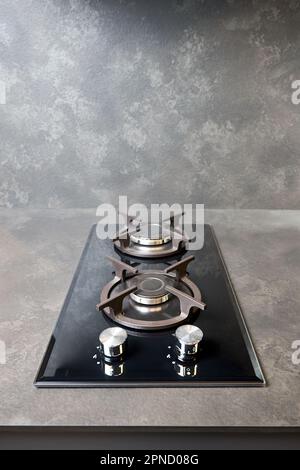 Table de cuisson contemporaine en verre trempé noir avec deux brûleurs avec bouton d'allumage automatique, supports de casseroles en fonte et valve de sécurité anti-flamme intégrée Banque D'Images