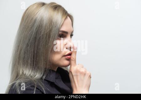 Belle jeune femme caucasienne isolée sur fond gris studio tenir le doigt sur les lèvres demander être silencieux, millénaire regarder la caméra dire Banque D'Images