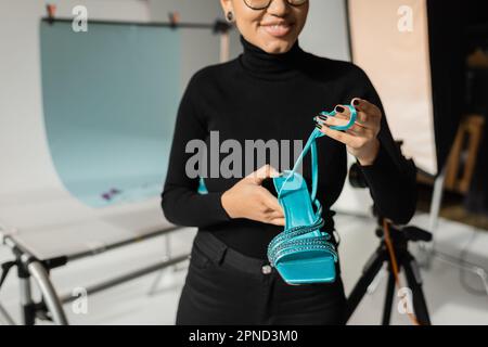 vue rognée du créateur de contenu afro-américain souriant en col roulé noir tenant le sable tendance dans un studio de photo flou, image de stock Banque D'Images