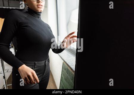 vue rognée du fabricant de contenu afro-américain dans le col de cygne près de la fenêtre et le rideau noir dans le studio de photo, image de stock Banque D'Images