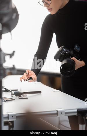 vue partielle du producteur de contenu afro-américain avec appareil photo numérique et mascara près de cosmétiques décoratifs sur la table de tournage en studio photo, stock im Banque D'Images