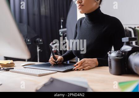 vue rognée de retouche afro-américaine à l'aide d'une tablette graphique tout en travaillant sur un ordinateur dans un studio photo, image de stock Banque D'Images