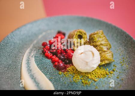 Gros plan de baklava pistache à la crème glacée à la vanille et aux baies fraîches, un dessert méditerranéen gastronomique pour les occasions spéciales Banque D'Images