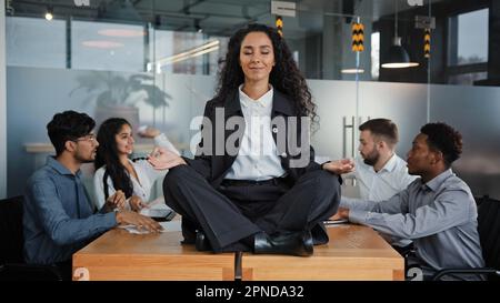 Femme d'affaires calme leader femme faisant de l'exercice de yoga de respiration prenant la pause méditant assis à table au bureau dans la réunion de fond de méditation Banque D'Images