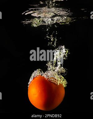 Tomate mûre tombe profondément sous l'eau avec un grand bruit. Banque D'Images