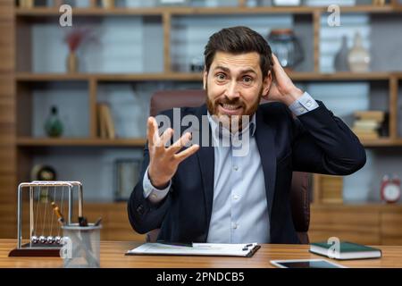 Un patron en colère hurlant à la caméra, un homme d'affaires chevronné travaillant dans un bureau, un homme d'affaires en costume d'affaires avec ordinateur portable nerveux et en colère. Banque D'Images