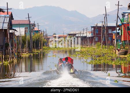 Un bateau en bois navigue parmi les maisons sur pilotis d'un village du lac Inle, dans l'État de Shan, au Myanmar. Banque D'Images