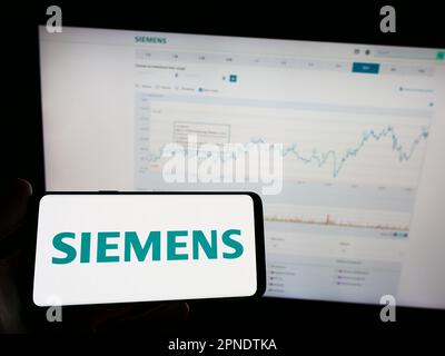 Personne tenant un téléphone portable avec le logo du conglomérat allemand Siemens AG sur l'écran en face de la page Web d'affaires. Mise au point sur l'affichage du téléphone. Banque D'Images