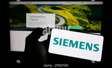 Personne tenant un téléphone portable avec le logo du conglomérat allemand Siemens AG à l'écran en face de la page web d'affaires. Mise au point sur l'affichage du téléphone. Banque D'Images