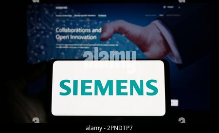 Personne tenant un smartphone avec le logo du conglomérat allemand Siemens AG à l'écran devant le site. Mise au point sur l'affichage du téléphone. Banque D'Images