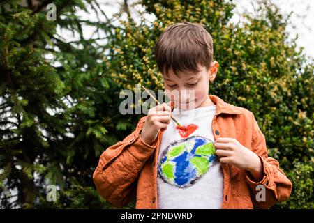 Concept de mode de vie durable. Un écolier dessine un globe terrestre sur un t-shirt. Énergie verte, ESG, ressources renouvelables, protection de l'environnement, protection de la planète Banque D'Images