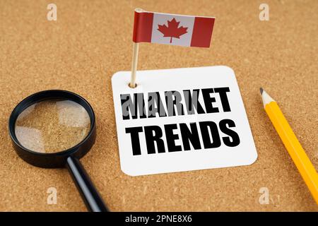 Sur la table se trouve le drapeau du Canada, un crayon, une loupe et une feuille de papier avec l'inscription - tendances du marché Banque D'Images