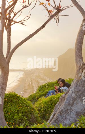 Un couple assis devant les falaises de Lima Malecon au coucher du soleil, Miraflores, Lima, Pérou. Banque D'Images