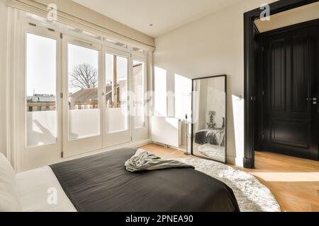 une chambre avec un lit noir et des draps blancs sur le sol, devant une grande porte coulissante en verre Banque D'Images
