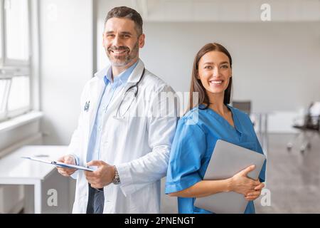 Équipe de deux médecins professionnels travaillant ensemble en clinique, homme posant avec une tablette numérique, femme avec un presse-papiers Banque D'Images