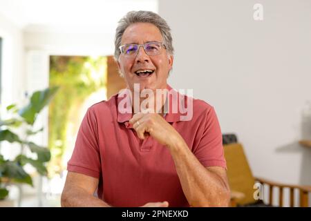 Portrait d'un homme âgé du caucase portant des lunettes de rire tout en étant assis contre le mur à la maison Banque D'Images