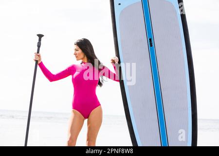 Femme tenant un char à côté du paddleboard sur la plage Banque D'Images