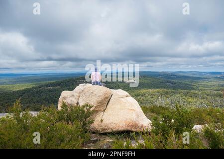 Australie, Nouvelle-Galles du Sud, parc national de Bald Rock, femme assise sur le rocher et regardant autour Banque D'Images