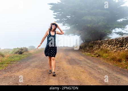 Femme touristique avec chapeau marchant à travers le chemin brumeux vers la forêt de genévrier à El Hierro. Îles Canaries Banque D'Images