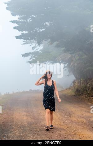 Femme touristique avec chapeau marchant à travers le chemin brumeux vers la forêt de genévrier à El Hierro. Îles Canaries Banque D'Images