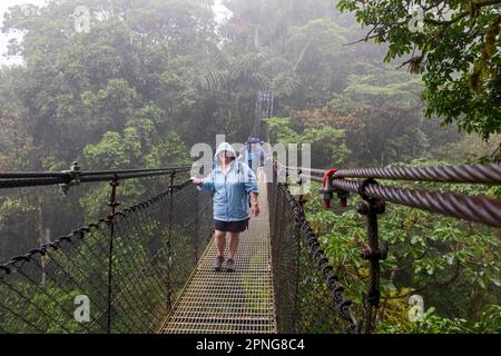 La Fortuna, Costa Rica, les touristes traversent un pont suspendu sous la pluie dans le parc Mistico Hanging Bridges. Le parc permet aux touristes de faire de la randonnée à travers le Banque D'Images