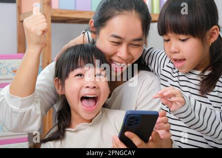 Mère et fille jouant et embrassant, prenant des selfies sur des smartphones, regardant des dessins animés ou jouant à des jeux en ligne à la maison. Bonne famille aimante et mot Banque D'Images