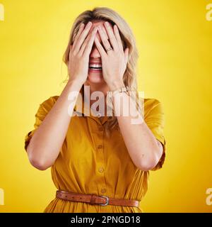 Comique, drôle et gêné avec une femme sur fond jaune en studio riant à une blague. Sourire, comédie et humour avec une personne qui apprécie le rire Banque D'Images