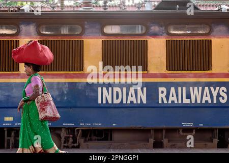 Une femme indienne portant un paquet de vêtements sur sa tête passe une voiture de chemin de fer indien; Chhatrapati Shivaji Maharaj Terminus, Mumbai, Inde Banque D'Images