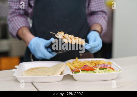 Le panier repas à emporter. Chef préparant un plat traditionnel grec kalamaki avec de la viande de porc grillée et des légumes Banque D'Images