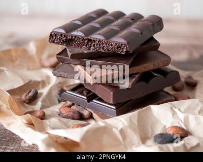 Morceaux de chocolat noir empilés sur la table en bois, mise au point sélective. Barres de chocolat et fèves de cacao Banque D'Images