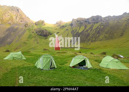 Vestmannaeyjar, Islande- août 2021 : tentes avec touristes dans un camping sur l'île de Vestmannaeyjar avec moulin rouge dans une vallée verdoyante Banque D'Images