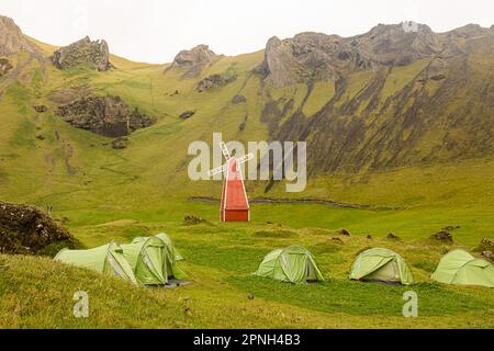 Vestmannaeyjar, Islande- août 2021 : tentes avec touristes dans un camping sur l'île de Vestmannaeyjar avec moulin rouge dans une vallée verdoyante Banque D'Images