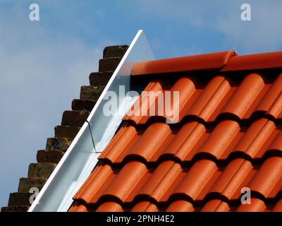 toit résidentiel incliné avec carreaux modernes en argile rouge. solin en métal galvanisé à l'extrémité du pignon vue détaillée. ciel bleu clair. construction de toit. Banque D'Images