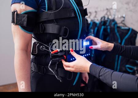 Les entraîneurs mains avec la manucure rouge aider à mettre sur ems costume à la cliente femelle dans le club de fitness. Jeune entraîneur définit les paramètres désirés sur la veste spéciale pour Banque D'Images