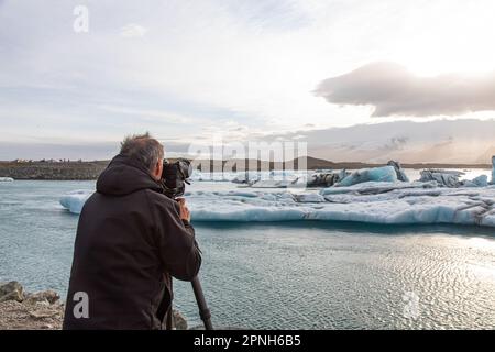 Jokulsarlon, Islande - 2021: Un photographe prenant une photo sur une vue spectaculaire au coucher du soleil de la baie de Jokulsarlon avec des icebergs flottant dans les eaux gelées Banque D'Images